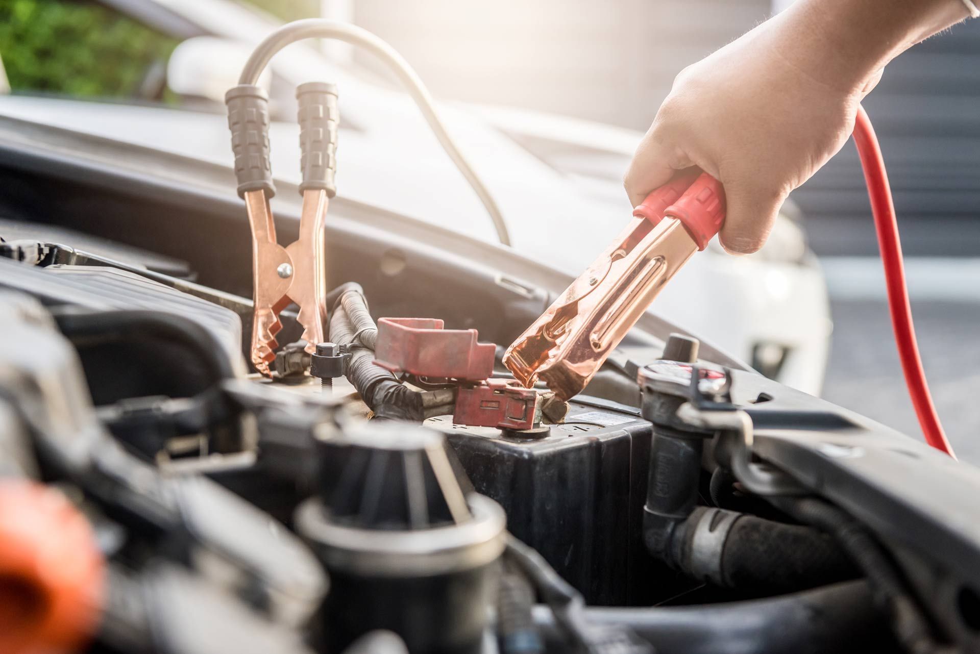 Connecting red jumper cable to a car battery's positive terminal; another cable connected to another vehicle's battery.