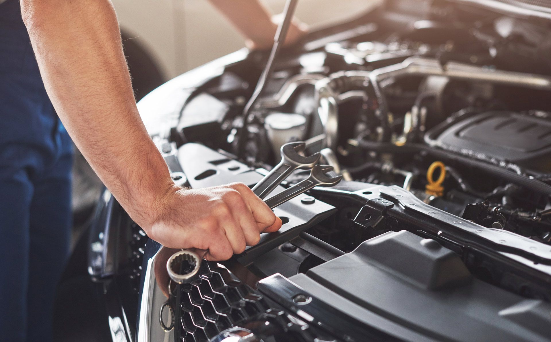 Mechanic working on a car engine with a wrench. The engine bay is open, lit, and a hand holds a wrench.
