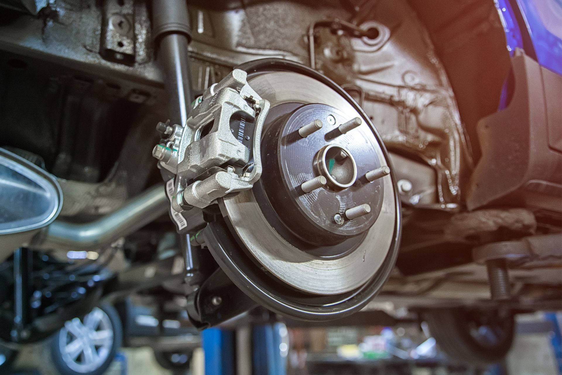 Car's rear brake disc and caliper assembly, showing the rotor, caliper, and suspension components, viewed from underneath.