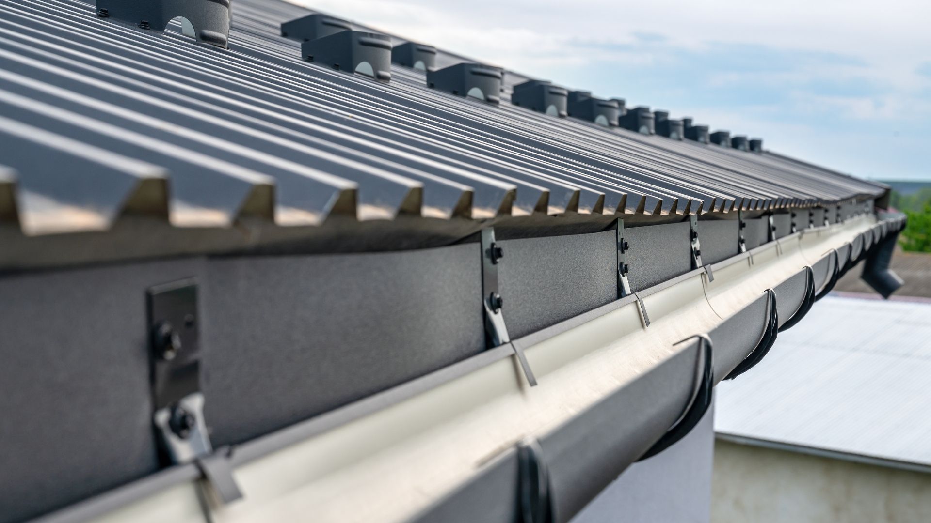 Metal corrugated rooftop and gutter system against a bright sky