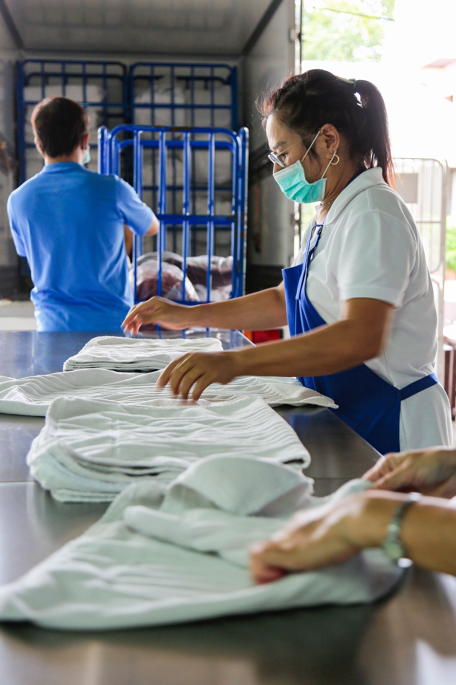 A woman wearing a mask is folding clothes on a table.