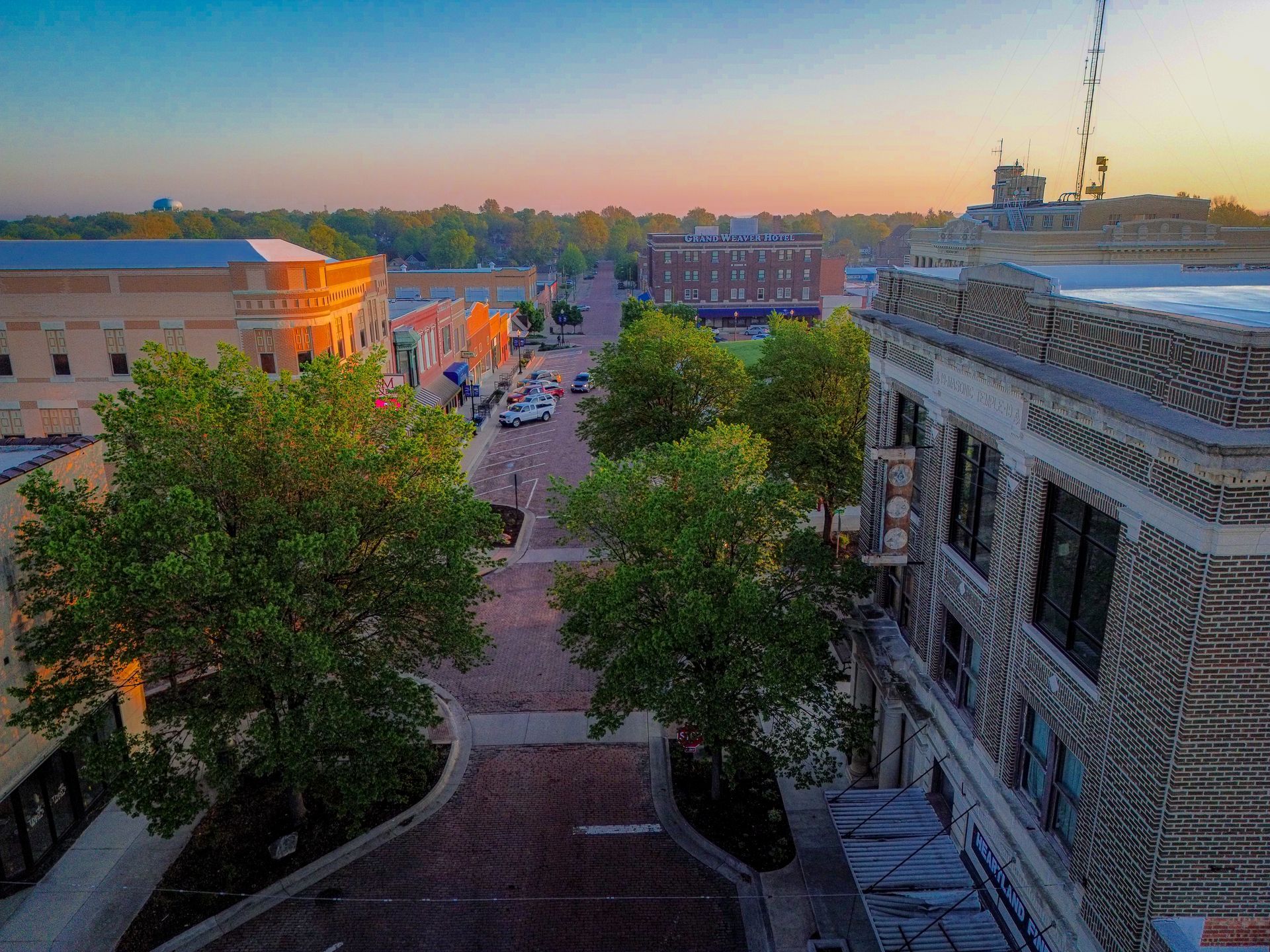 An aerial view of a city street with trees and buildings at sunset.