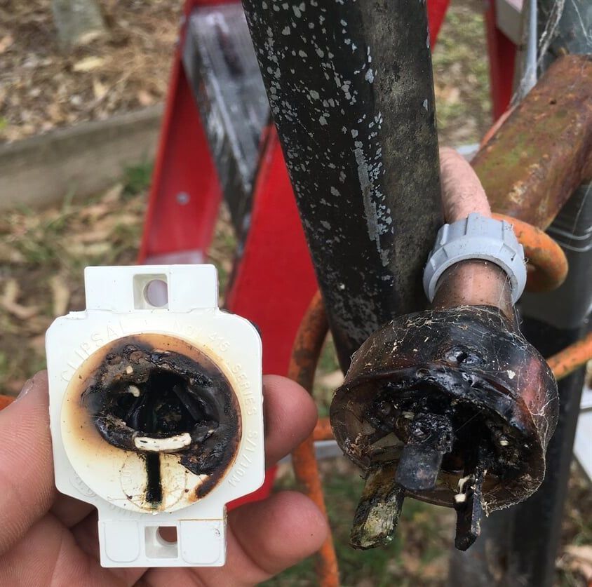A person is holding a burnt power plug — DG Electrical & Fire In Kiama, NSW
