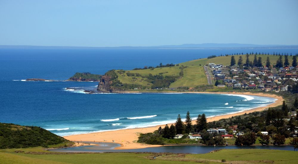 A Beach with mountains and houses— DG Electrical & Fire In Gerringong, NSW
