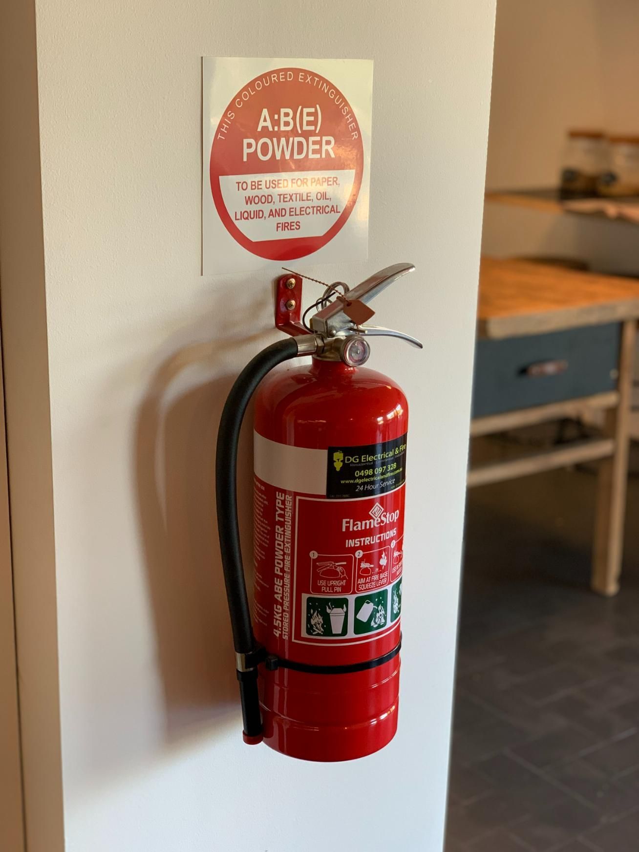 A Fire Extinguisher Is Hanging On A Wall Next To A Sign — DG Electrical & Fire In Kiama, NSW