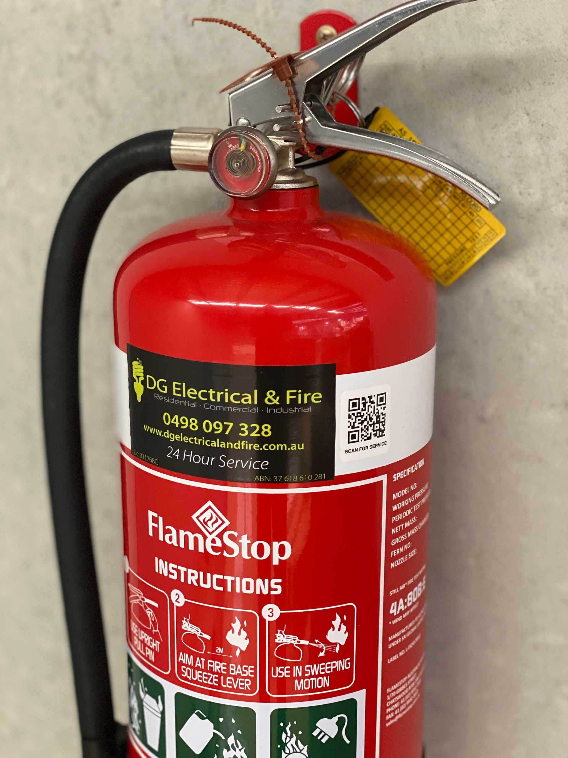 Red fire extinguisher hanging on a wall with black hose and yellow safety tag. — DG Electrical & Fire In Kiama, NSW