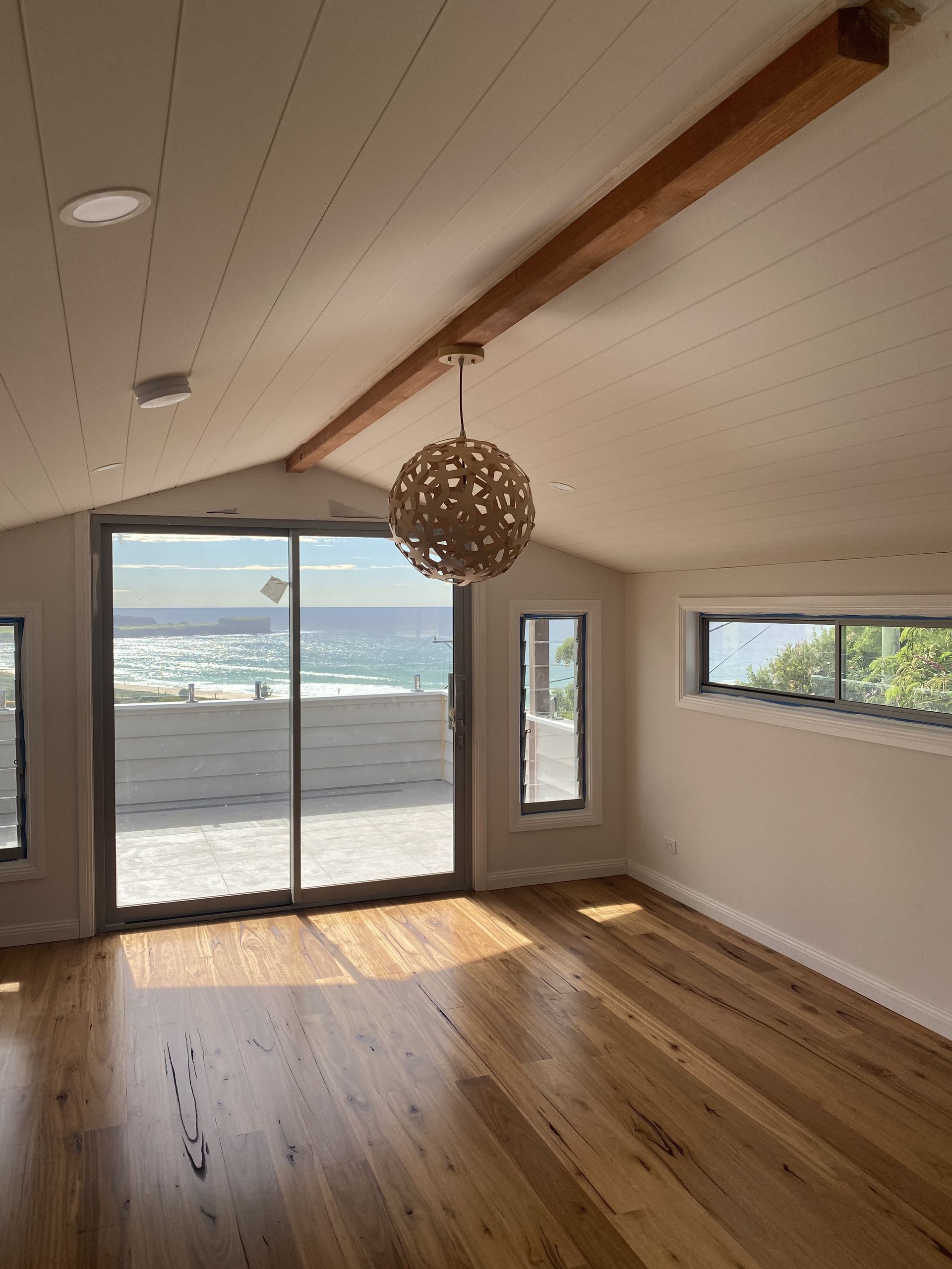 Bright Room With Ocean View, Sliding Glass Door, Wooden Floor and Ceiling, Pendant Light — DG Electrical & Fire In Kiama, NSW