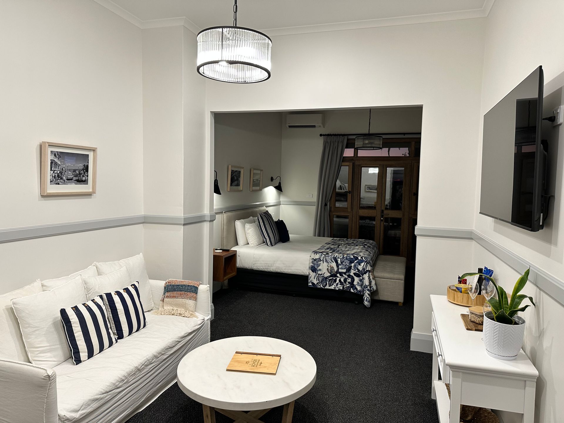 Living Area With White Sofa, Round Table, and Open Doorway to Bedroom With Bed — DG Electrical & Fire In Shoalhaven, NSW
