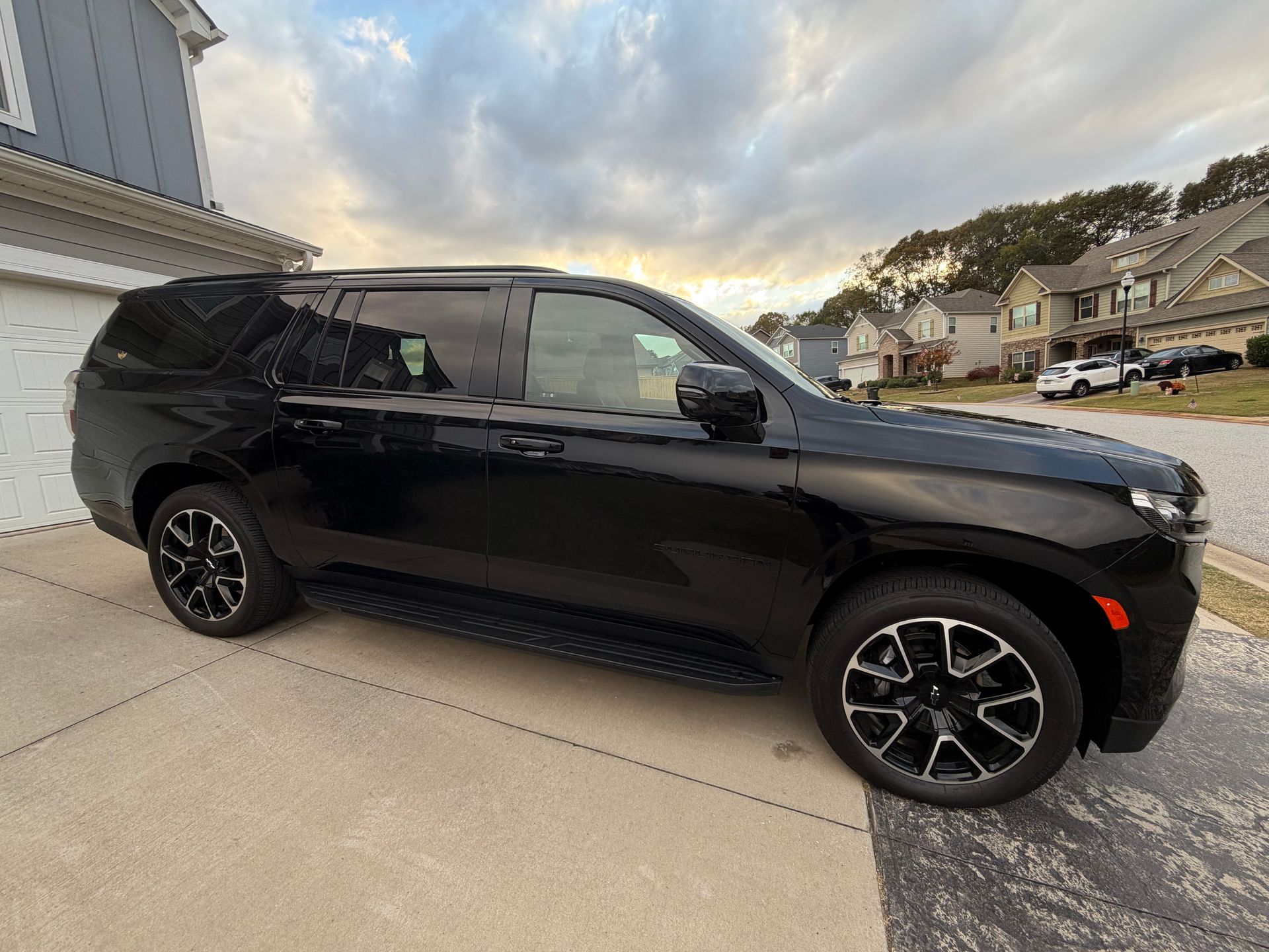 Black SUV parked on a driveway in front of a house. Cloudy sky overhead.
