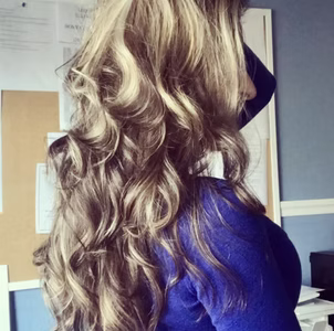 Long, wavy blonde hair cascading down a person's back; blue shirt, neutral background.