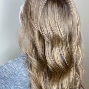 Woman with long, wavy blonde hair; a light blue top; facing away from the camera.