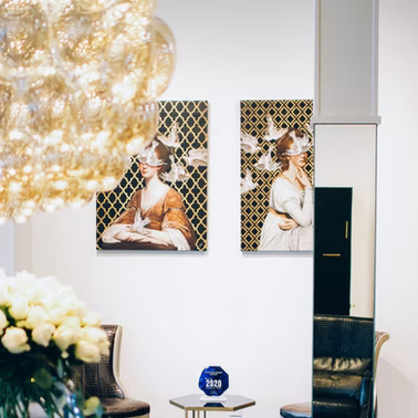 Two paintings of women with blindfolds and doves on a gold patterned background. Floral chandelier and furniture visible.