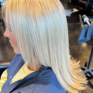 Woman with straight, light blonde hair. She is wearing a blue smock.