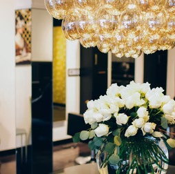 White roses in glass vase under a bubble chandelier in a stylish interior.