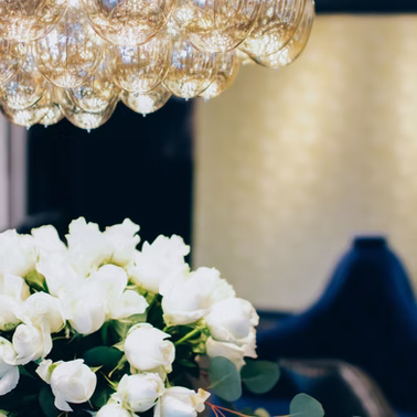White roses, vase, dark blue background, and ornate golden light fixture.