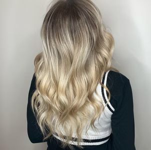 Woman with long wavy blonde hair, wearing a dark sweater with a white vest.