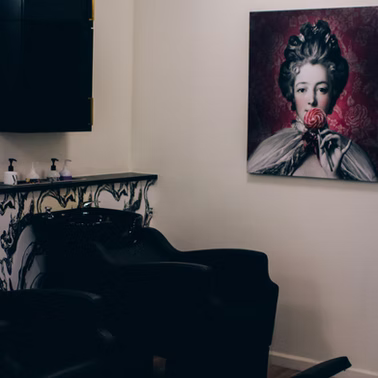 Salon wash station with black chairs, marble sink area, and artwork of a woman holding a rose.