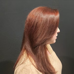 Woman with long, reddish-brown hair, side profile against a dark background, wearing a tan top.