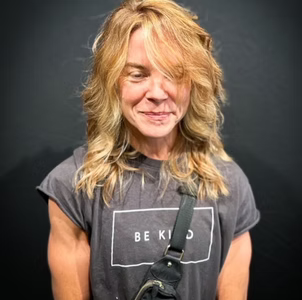 Woman with wavy blonde hair, wearing a gray t-shirt with 