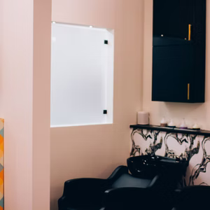 Salon interior with a white glass wall, black cabinet, and a hair-washing chair.