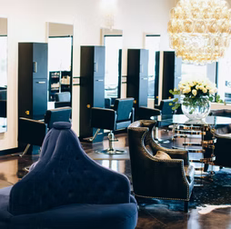 Salon interior with black and gold styling stations, blue chairs, and a chandelier.