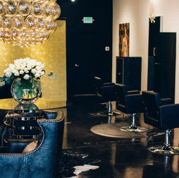 Upscale hair salon interior with black chairs, gold accents, and a large chandelier.