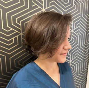 Woman with brown layered hair, wearing a blue shirt, in front of a geometric wallpaper.