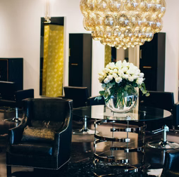 Elegant hair salon interior with a chandelier, floral arrangement, black chairs, and mirrors.
