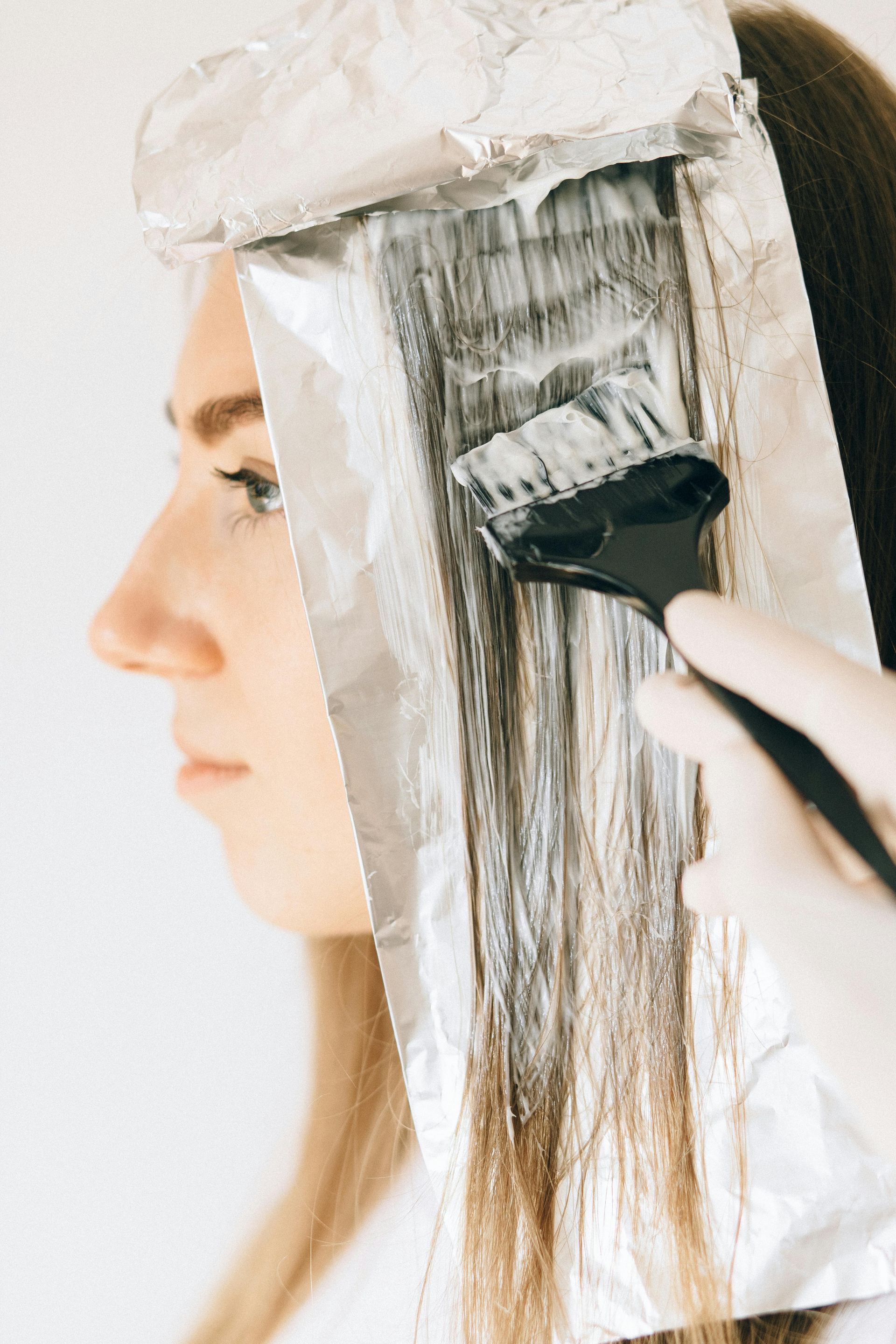 Person getting hair highlighted; foil wraps, brush applying bleach, side view.
