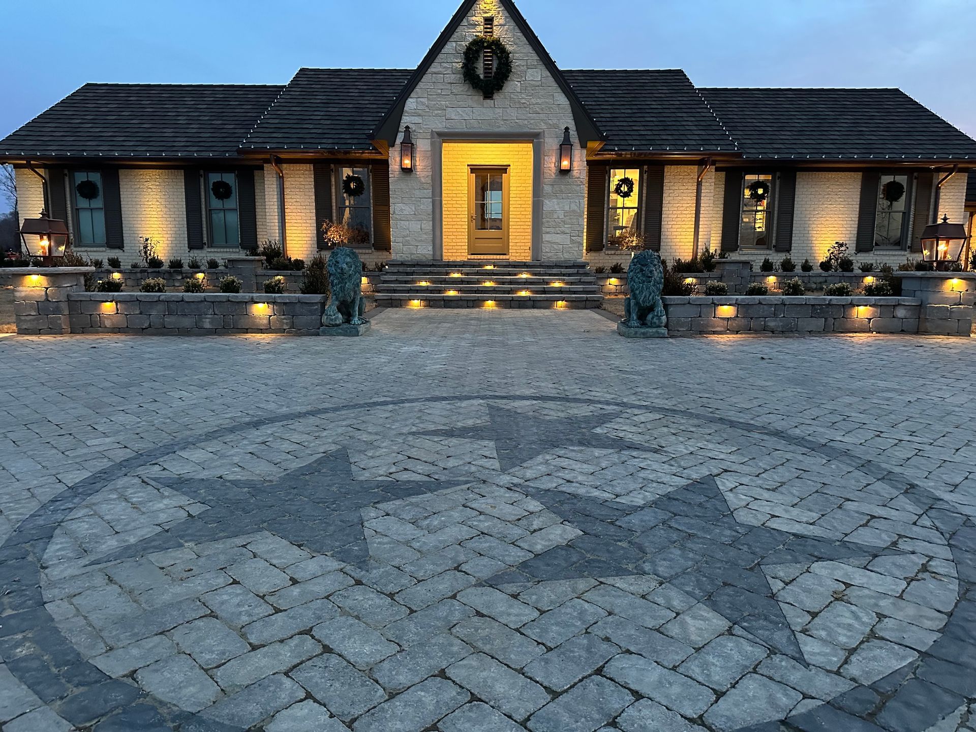 Stone house with Tennessee state flag pavers in driveway, lit up at dusk.