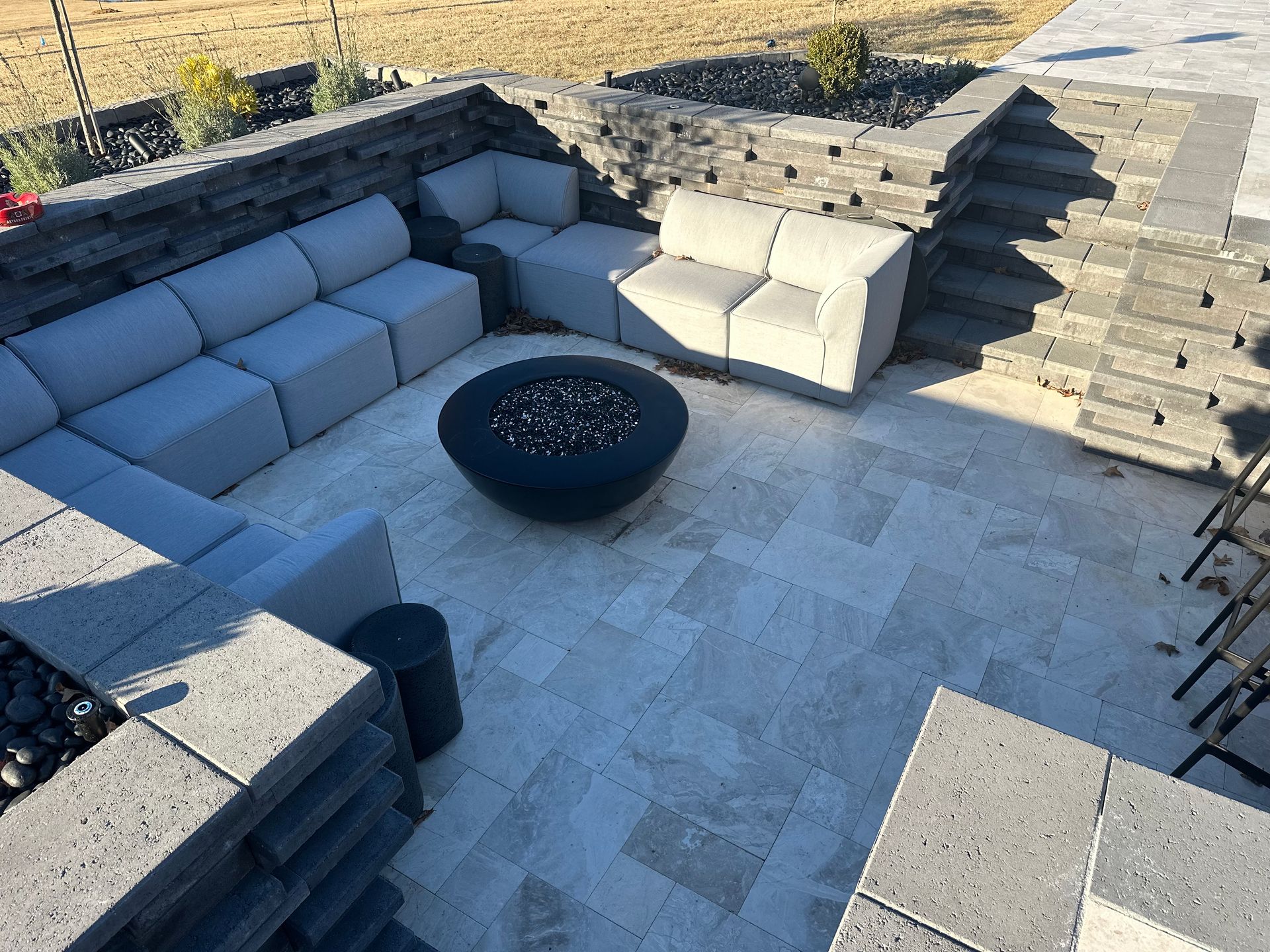 Outdoor patio with gray modular seating, fire pit, and stone walls.