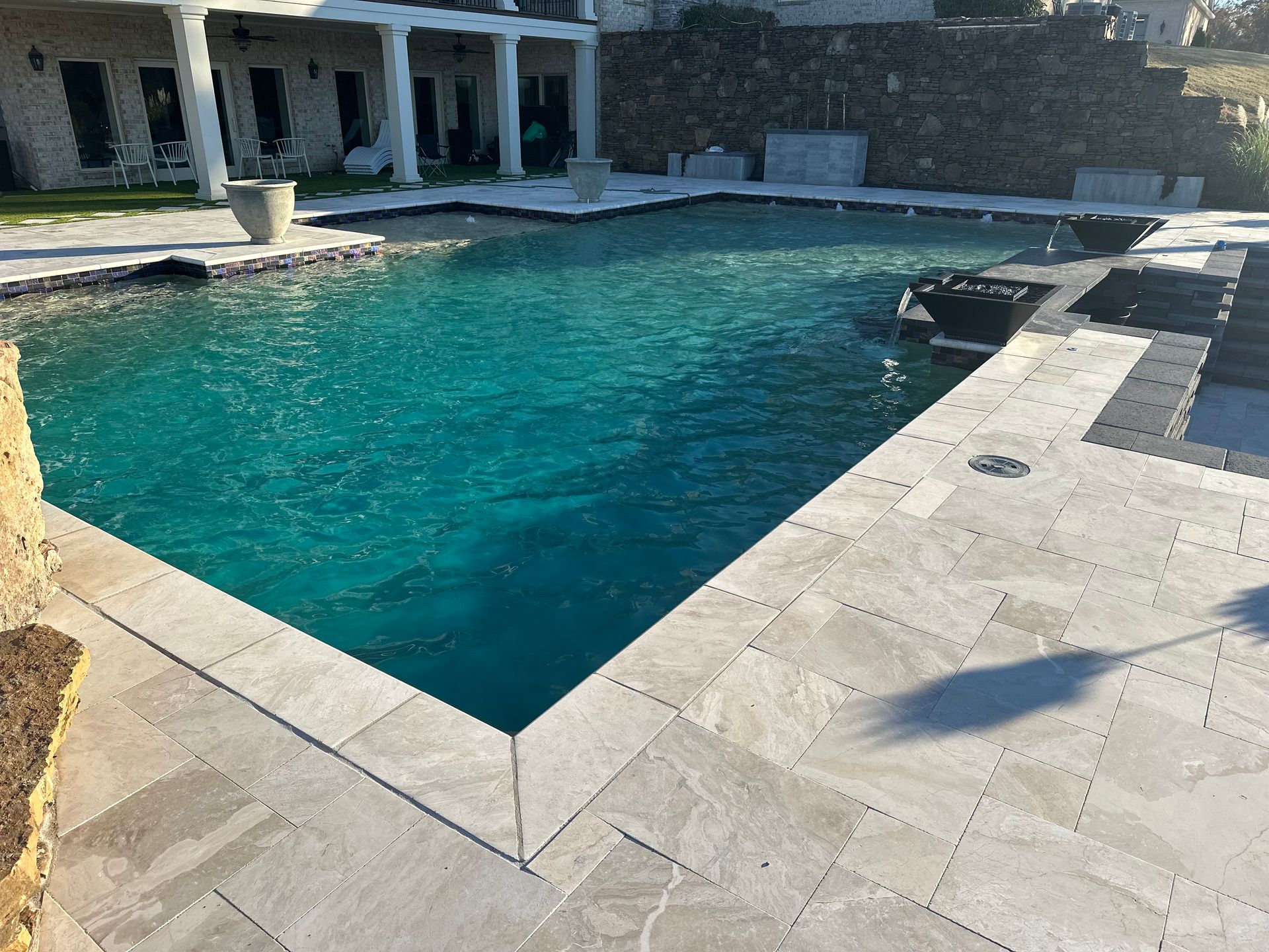 Swimming pool with turquoise water, surrounded by light stone patio and a stone wall.