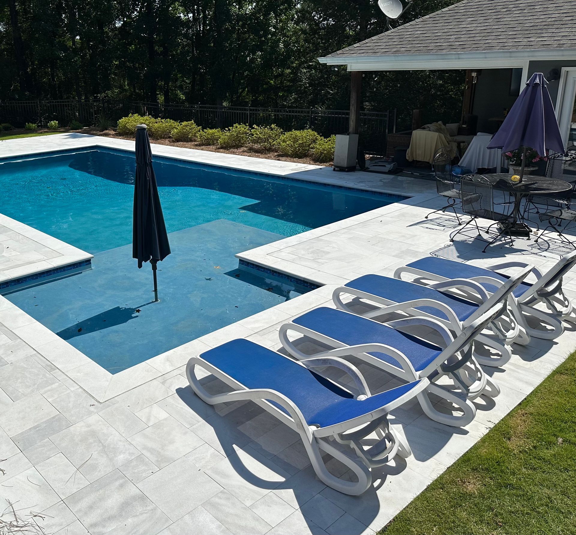 Swimming pool with blue water, lounge chairs, and an umbrella, sunny outdoor setting.