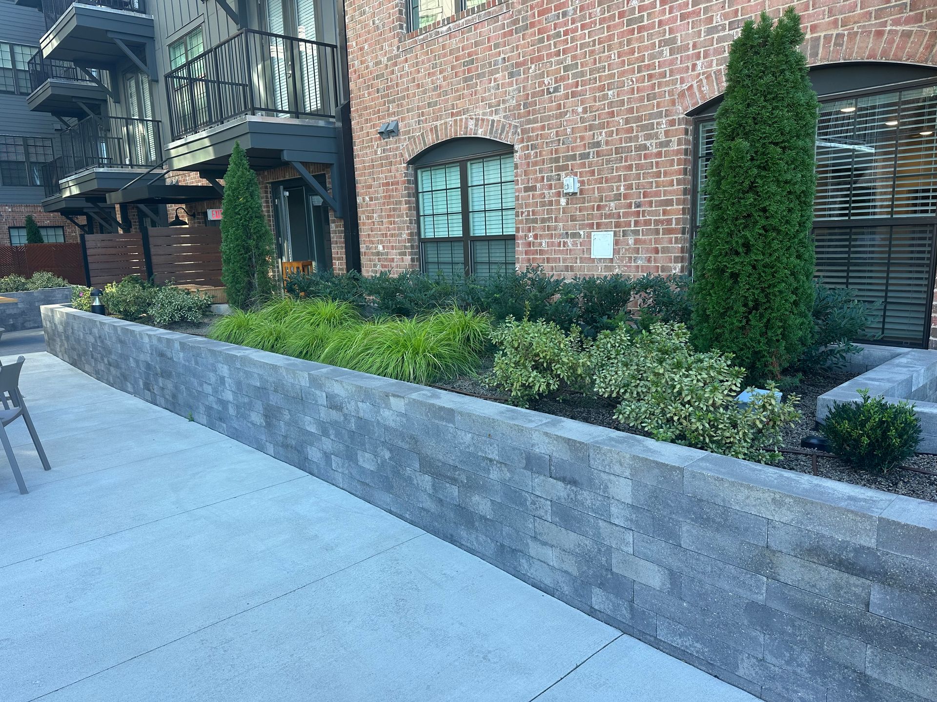 Brick building with a raised planter box. Green plants and two tall, slender trees are in the planter.