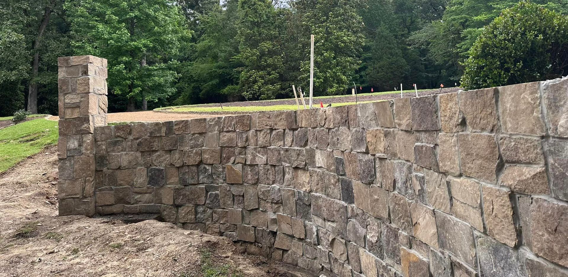 Stone wall in front of greenery. A pillar is at the corner of the wall.