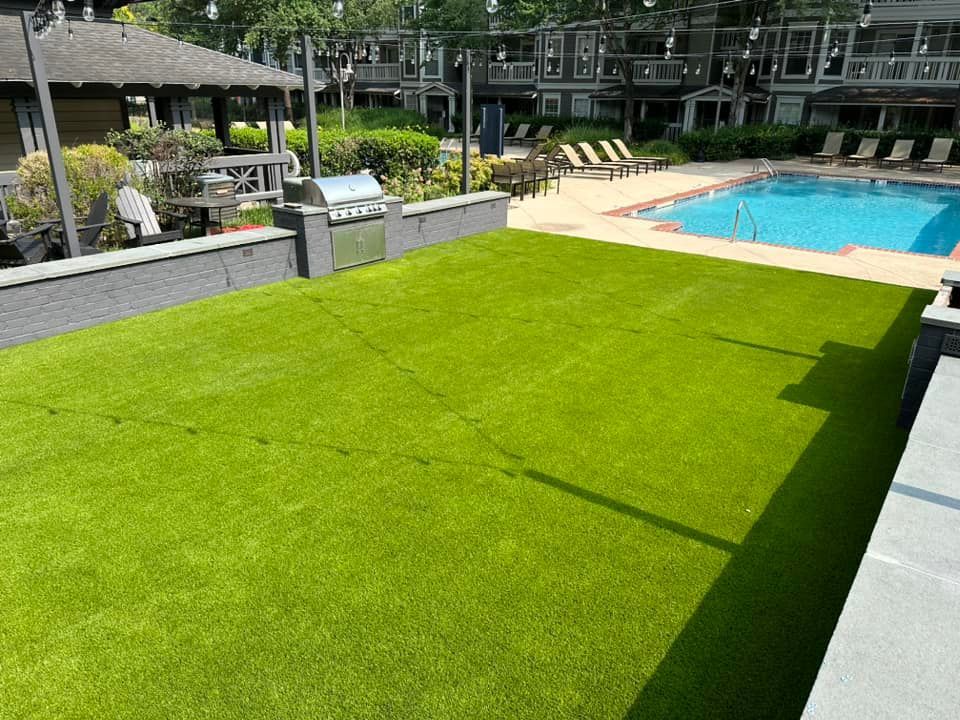 Lush green artificial turf area next to a swimming pool and outdoor dining space.