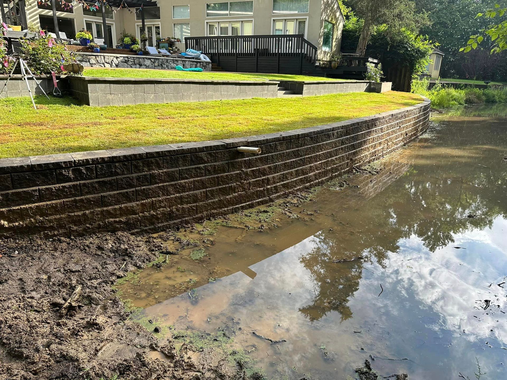 Stone retaining wall next to a murky body of water, with a grassy area above.