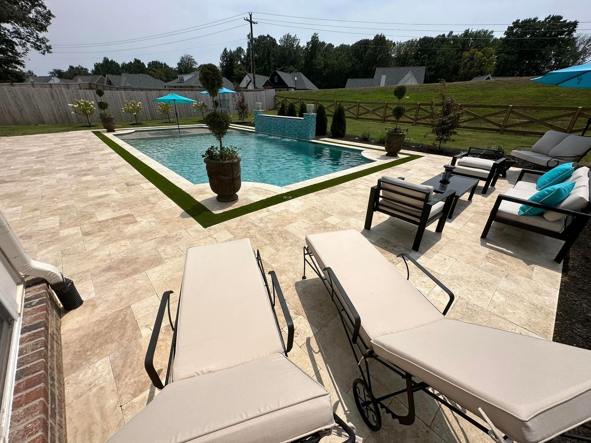Backyard with pool, lounge chairs, and seating area on a paved patio.