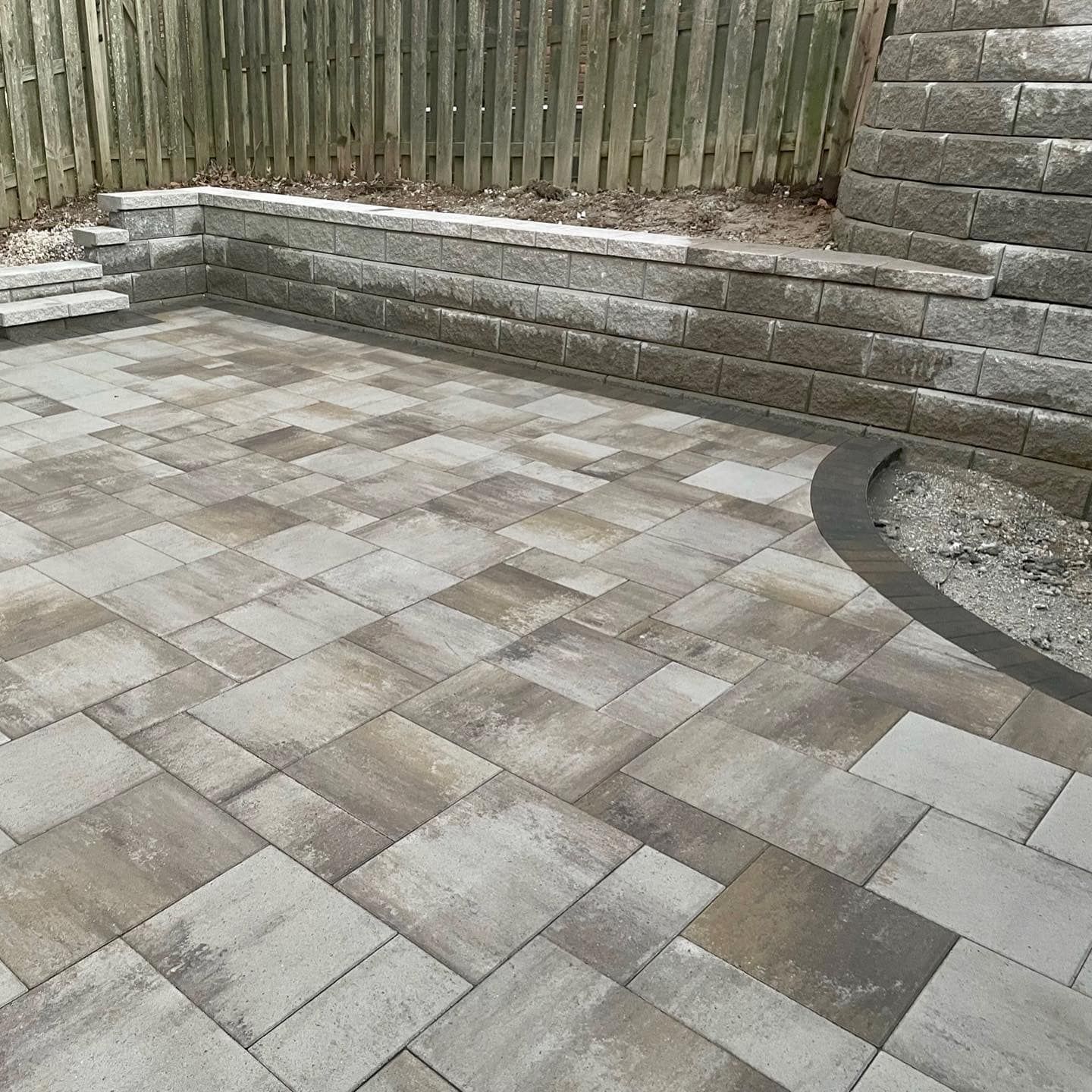 Paver patio with retaining wall and fence backdrop; gray and brown tones.