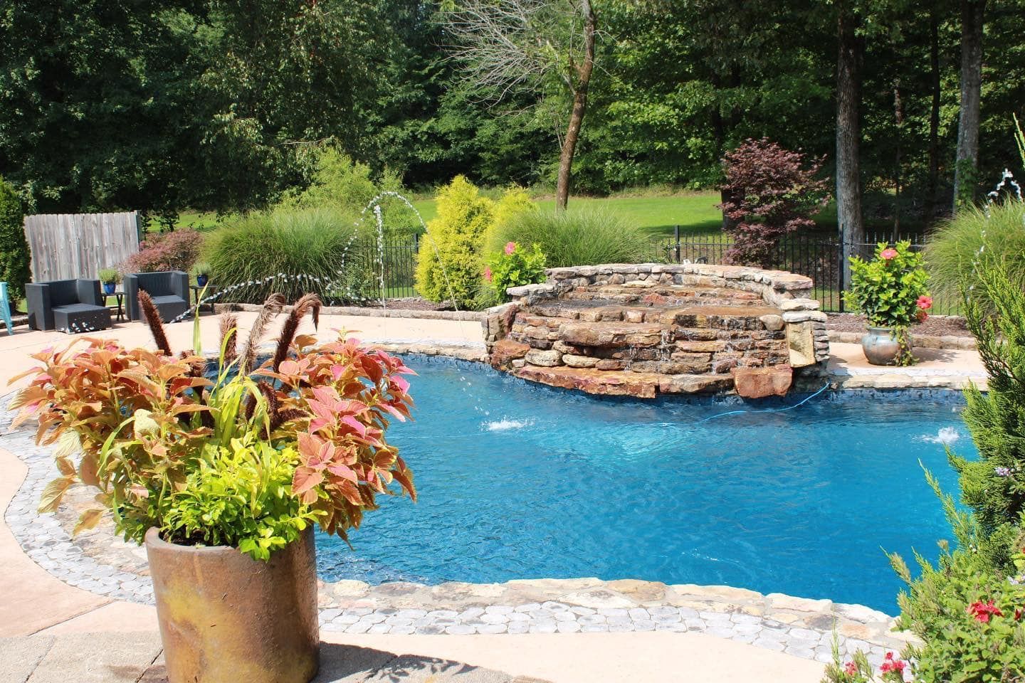 Pool with stone waterfall, surrounded by lush greenery and patio.