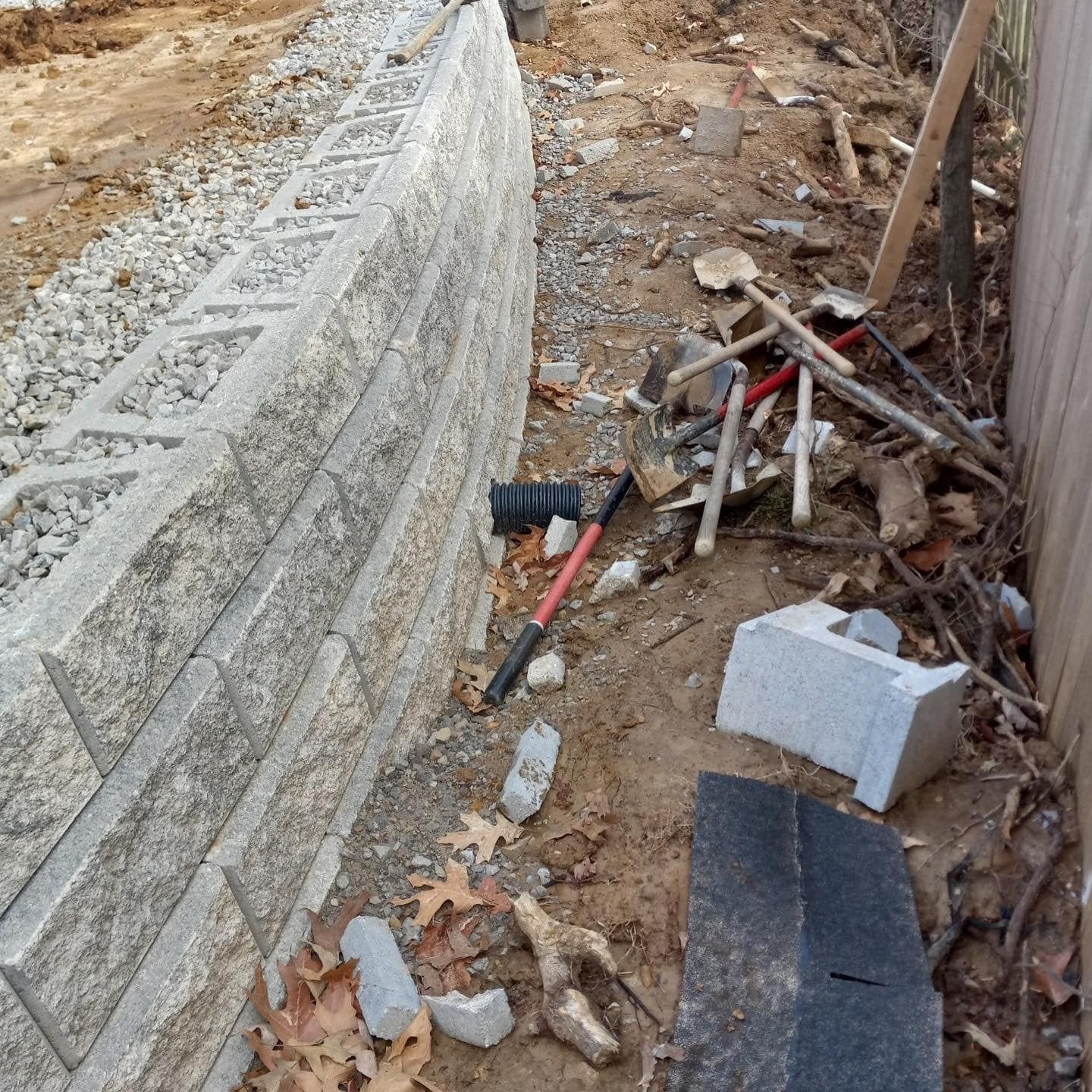 Retaining wall made of concrete blocks, construction tools and debris nearby.