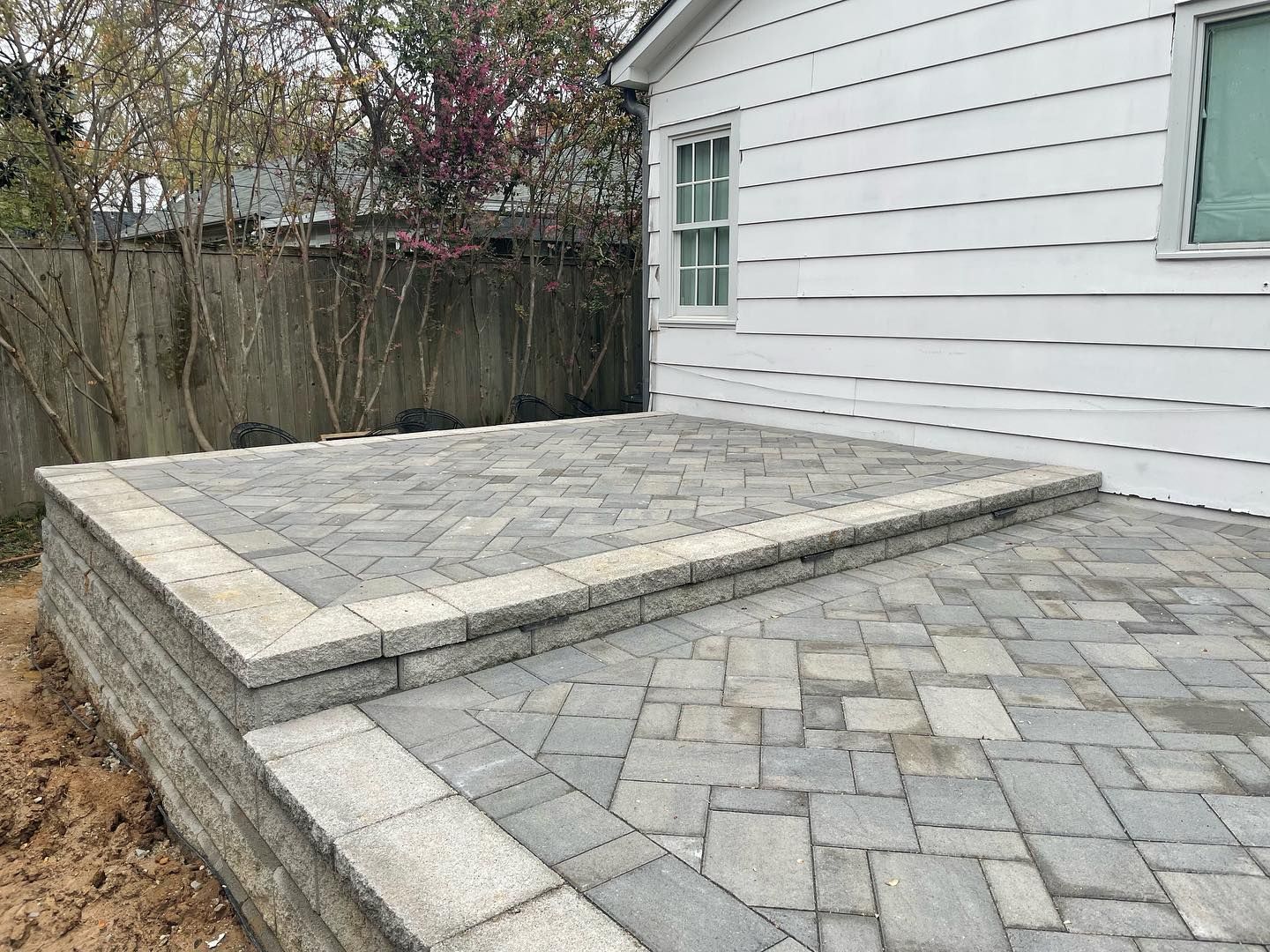 Brick patio and retaining wall next to a white house.