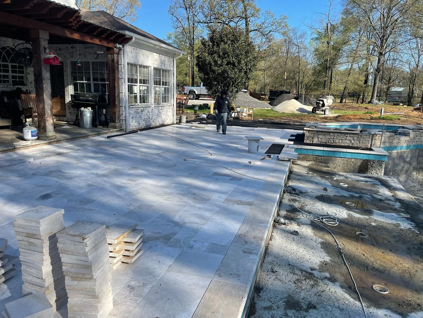 Patio being constructed with stone pavers near a pool and a house.