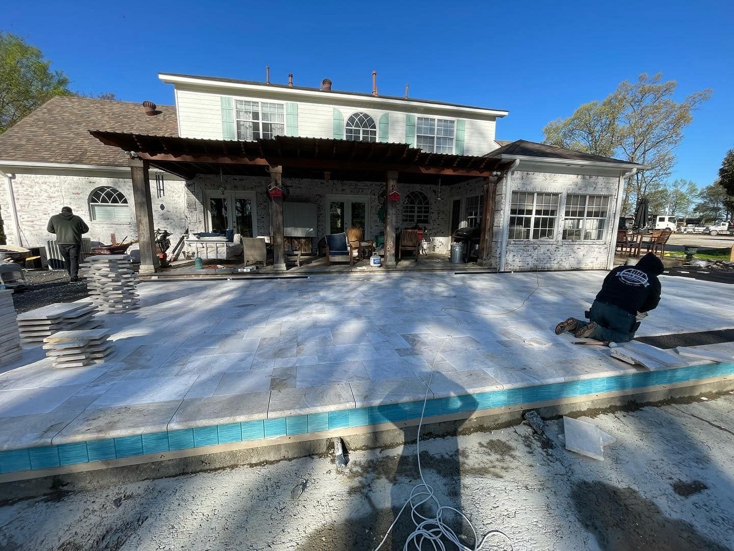 Workers laying pavers around a pool at a home with a pergola.