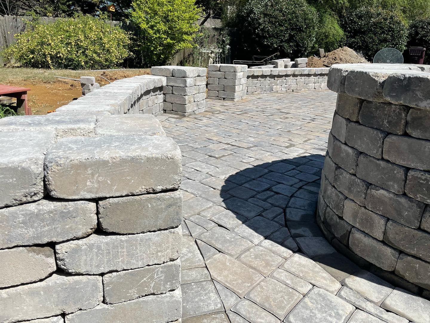Stone patio and low walls with curved design, brick pavers, in outdoor setting.