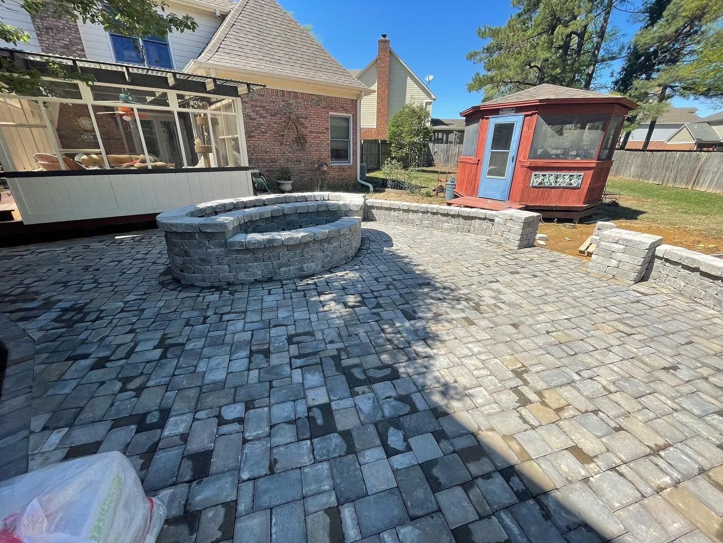 Brick patio with a fire pit and small red shed in a backyard setting.