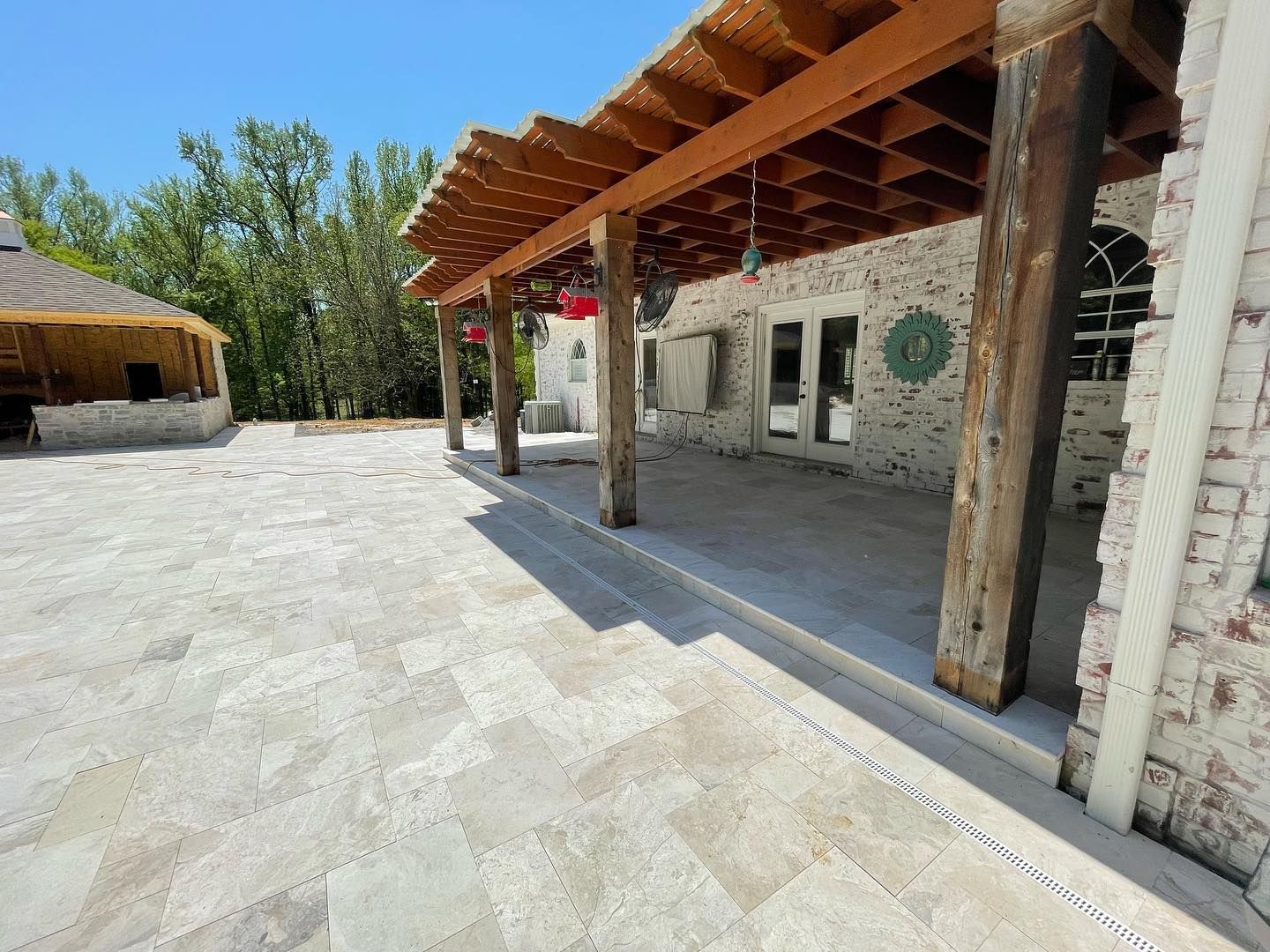 Patio with wooden beams, brick wall, and decorative roof, on a sunny day.