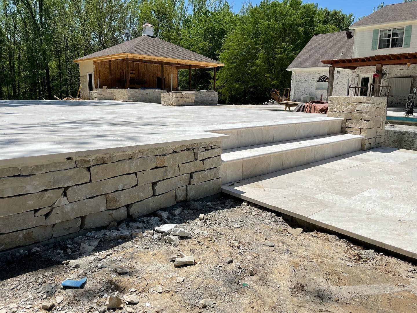 Stone patio with steps and gazebo under construction next to a house.