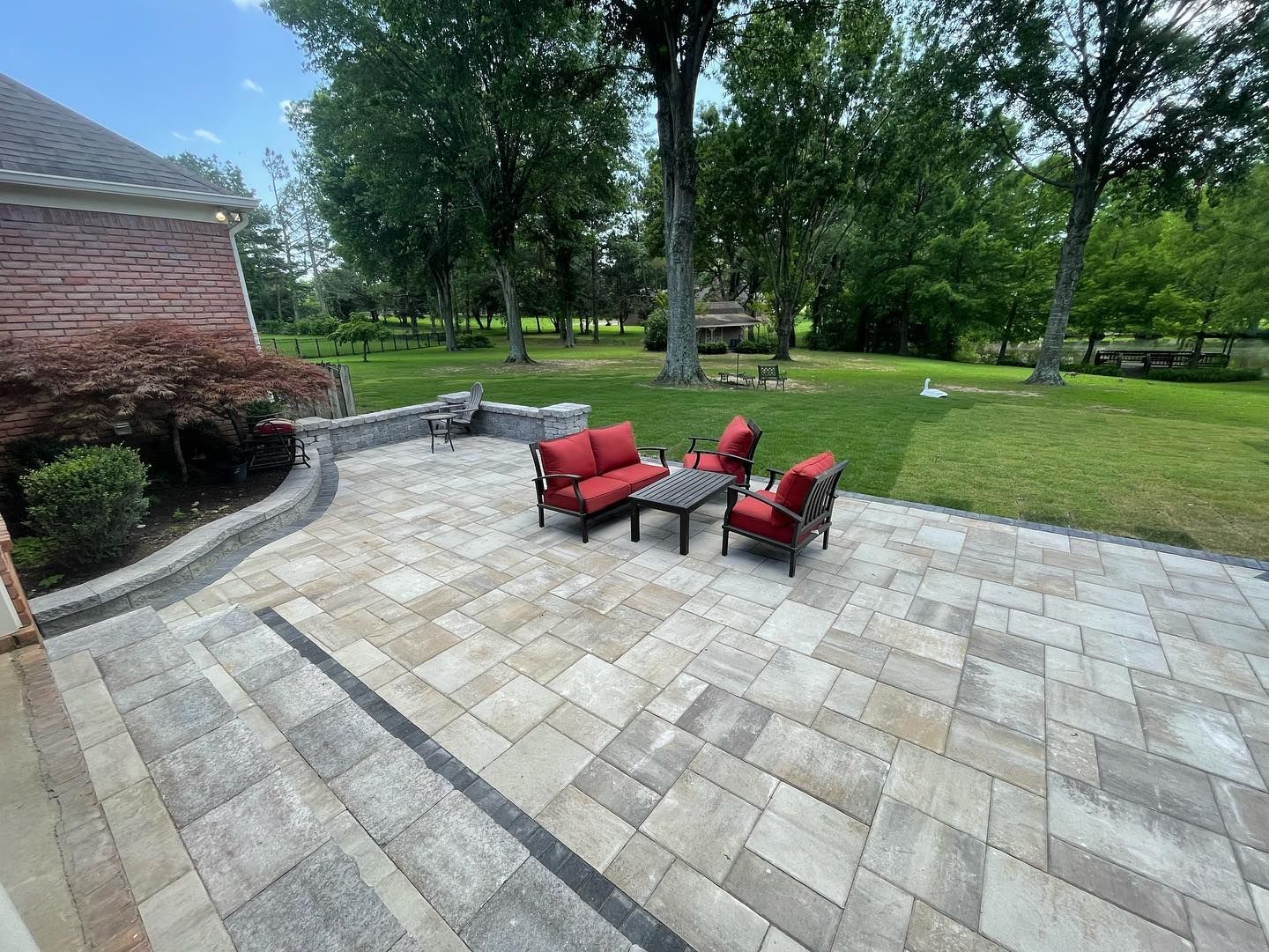 Patio with brick house, seating area with red cushions, and backyard with trees.