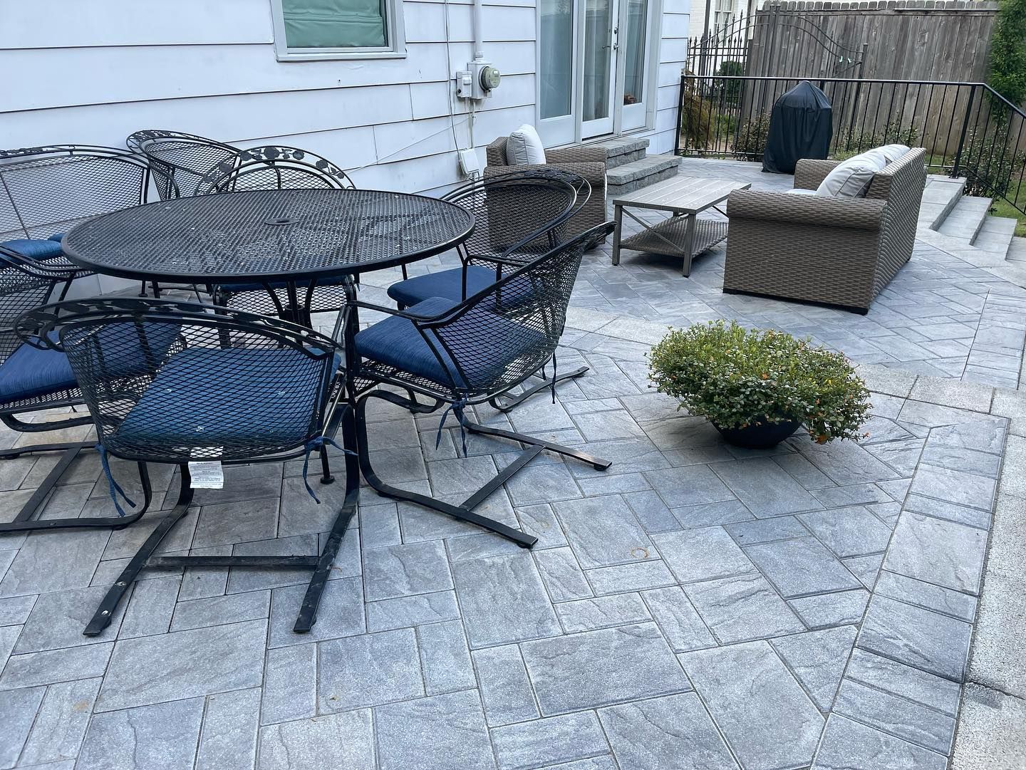 Patio with black metal table and chairs, gray pavers, and wicker furniture.